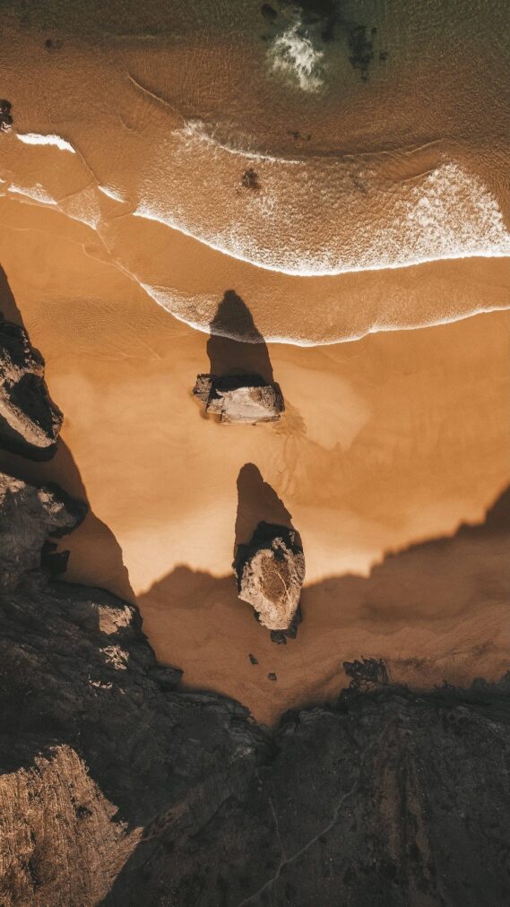 Aerial drone view showcasing golden cliffs and turquoise waters of a typical Algarve beach near POMAR Coliving, Portugal