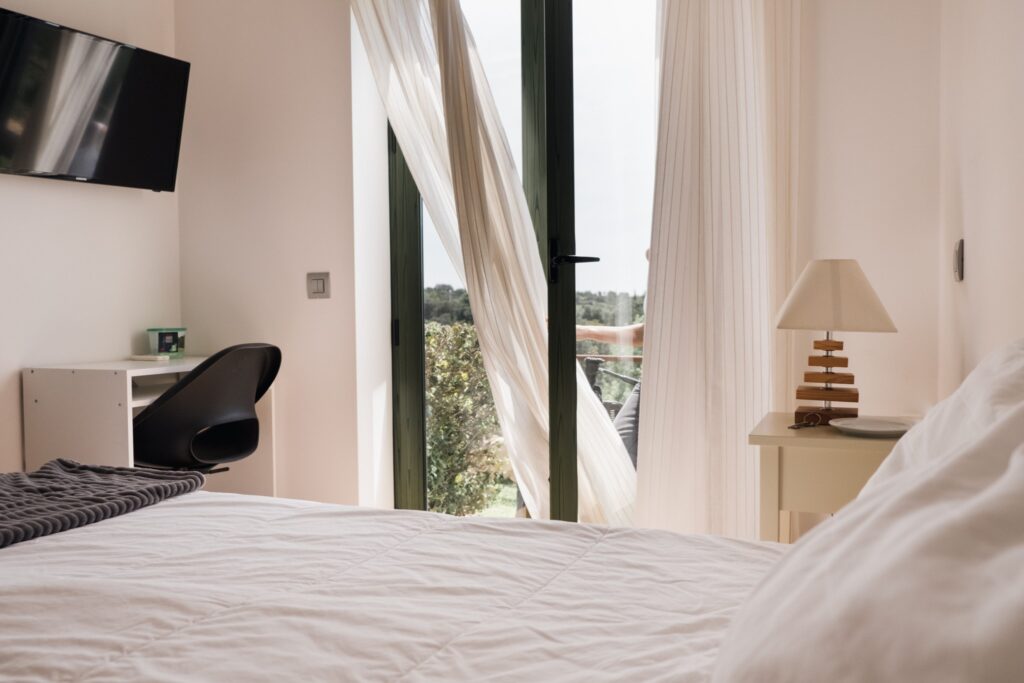 View of the double bedroom with private bathroom with a bed, a desk with ergonomic chair and glass door overlooking the garden.