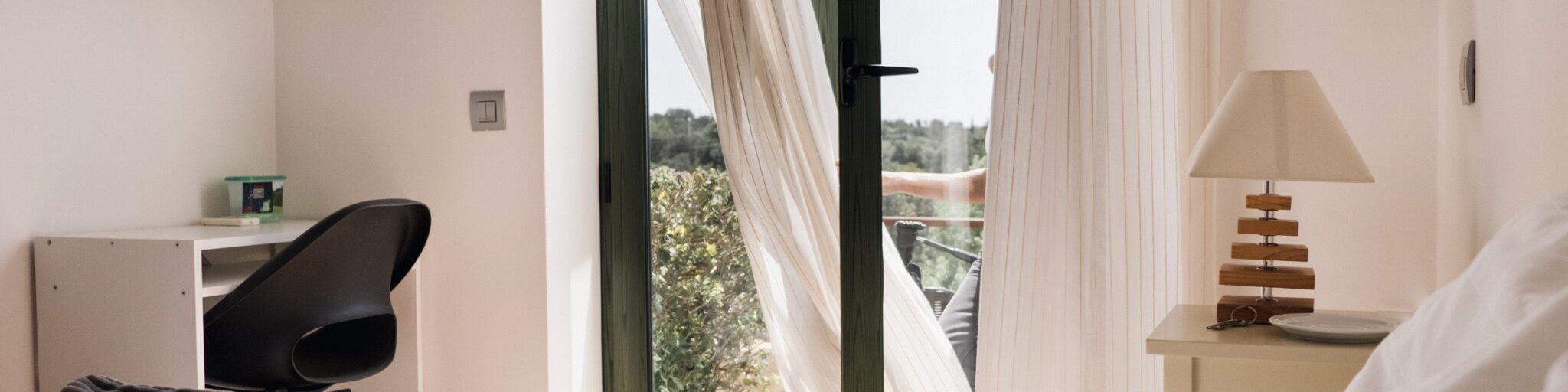 Double bedroom with private bathroom – main view – POMAR coliving View of the double bedroom with private bathroom with a bed, a desk with ergonomic chair and glass door overlooking the garden.