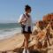 Farah’s testimonial – POMAR coliving Farah, a digital nomad and coliver at POMAR Coliving, standing on a cliff overlooking Praia da Marinha, Algarve, Portugal