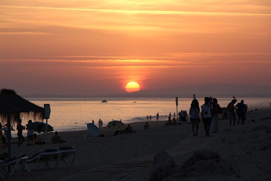 People looking at the beautiful sunset on the beach of Praia de Faro in Portugal.