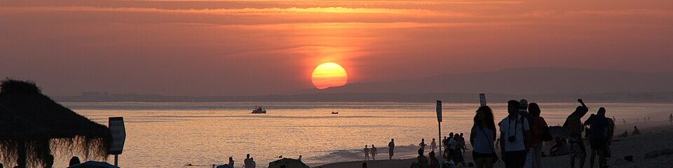 People looking at the beautiful sunset on the beach of Praia de Faro in Portugal.