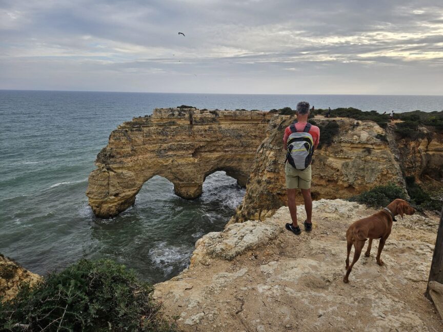 Man and dog enjoying a peaceful moment facing the sea atop the scenic cliffs of Benagil in Algarve, Portugal