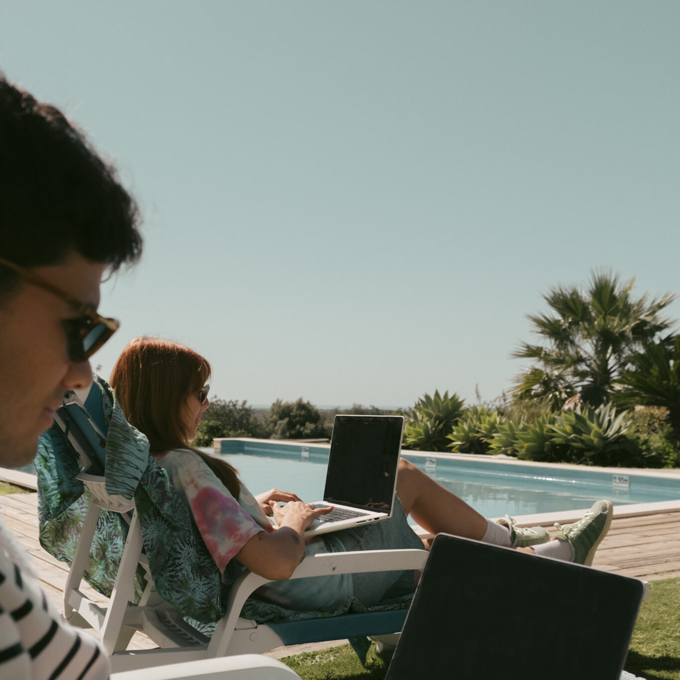 Remote workers using laptops poolside at POMAR Coliving in the Algarve