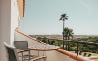 Private balcony with table and chairs overlooking palm trees and the Ria Formosa from POMAR na praia.