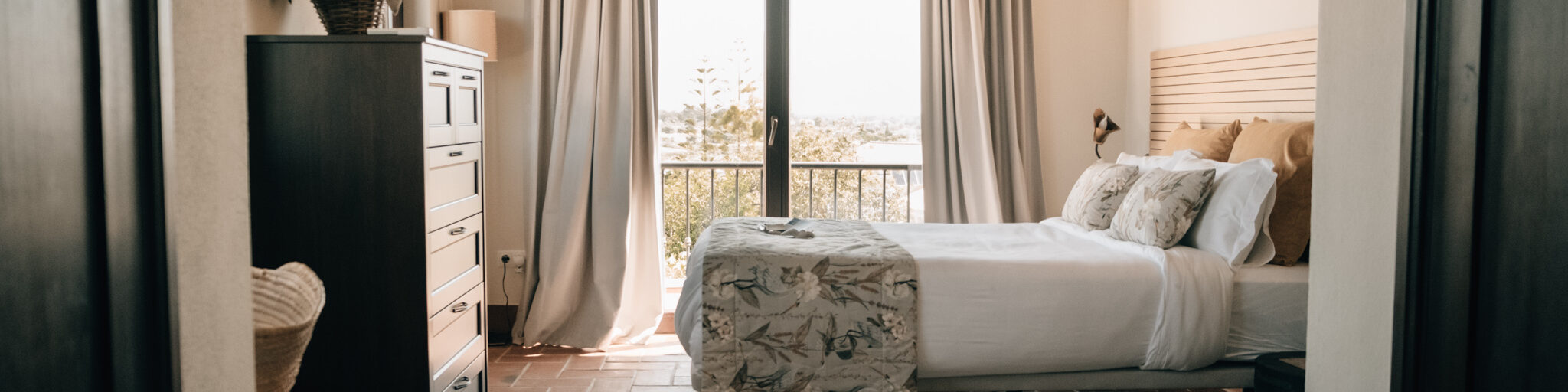 ground floor suite – POMAR na praia Elegant ground-floor suite at POMAR na praia with large bed, light curtains, terracotta floors, and balcony view.