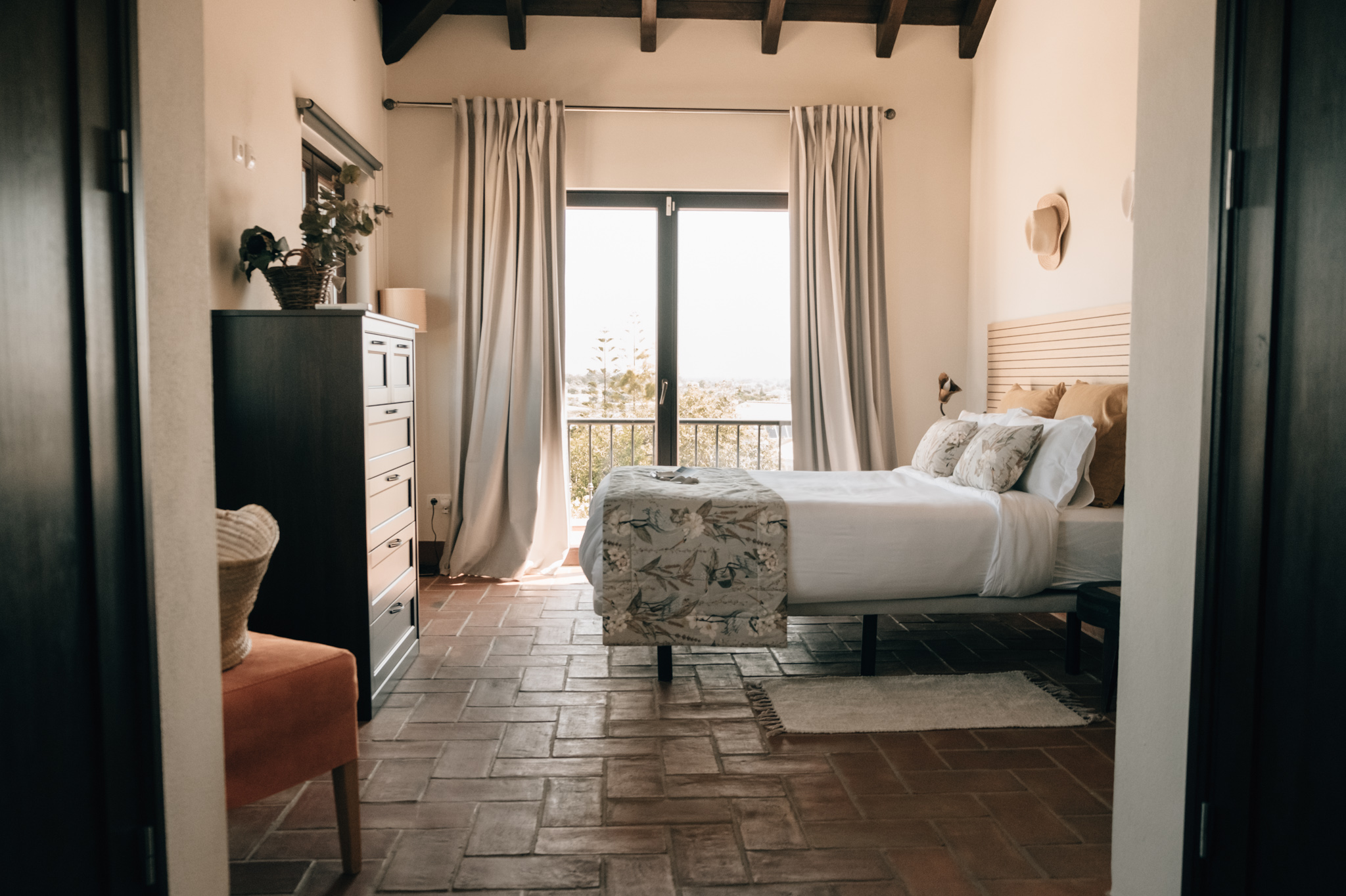 ground floor suite – POMAR na praia Elegant ground-floor suite at POMAR na praia with large bed, light curtains, terracotta floors, and balcony view.