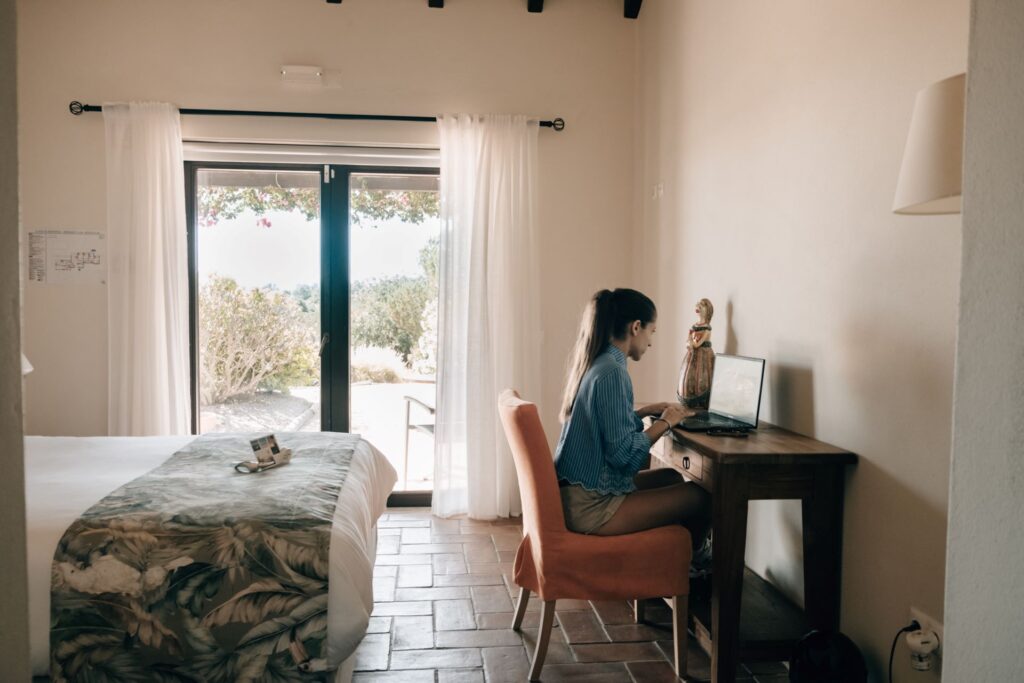 Woman working remotely from a wooden desk inside the suite at POMAR na praia with garden view.