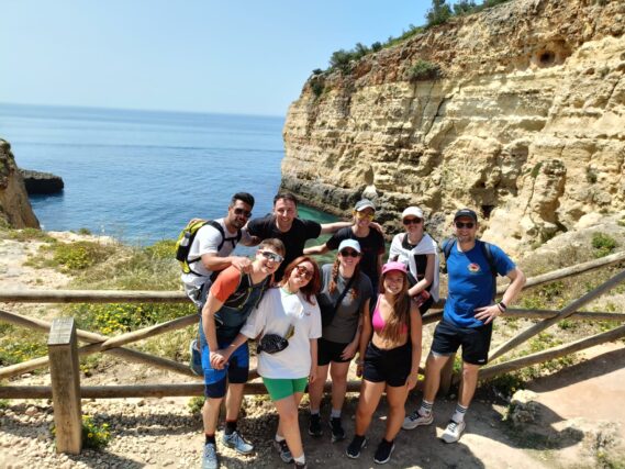 Group of smiling colivers standing on cliffs above the ocean during a hike near POMAR na praia
