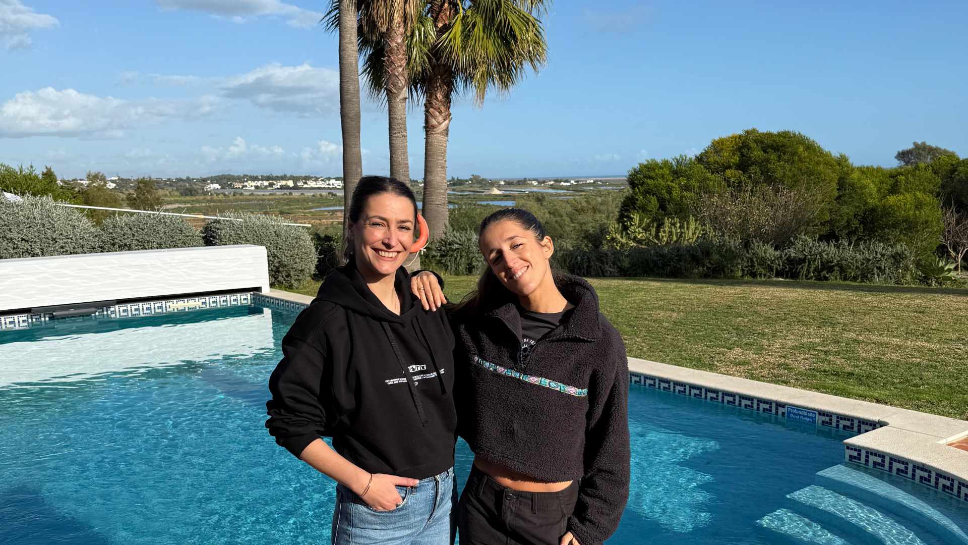 Two people standing together by the pool at POMAR Coliving with nature in the background