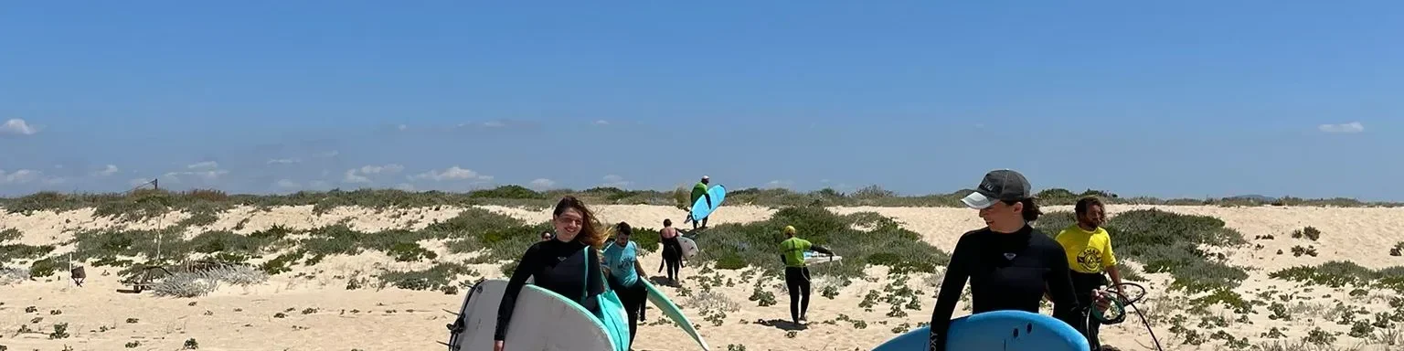 Group of people carrying surfboards across sand dunes toward the ocean