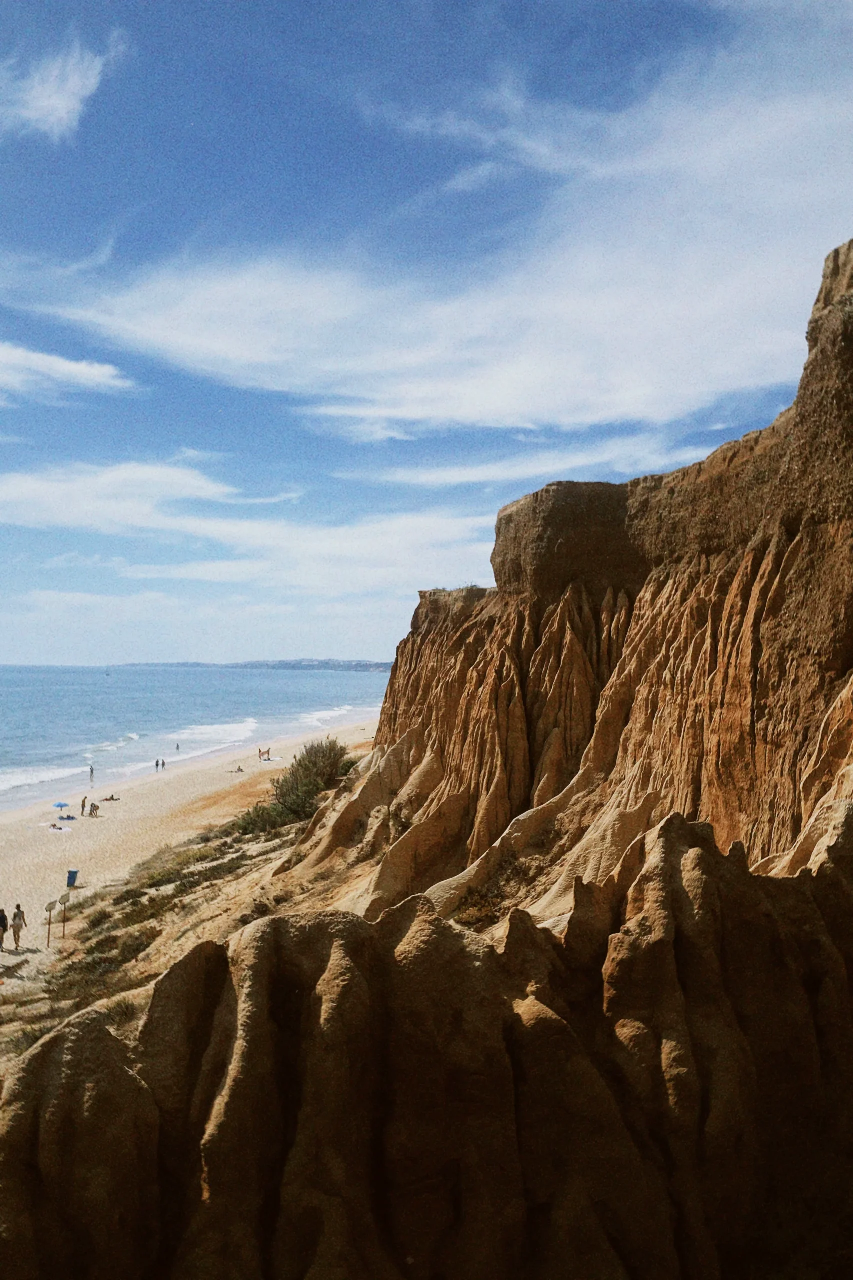 View from a rocky coastal cliff over a sandy beach and calm water.
