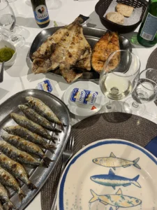 Grilled fish dishes, bread, condiments, and glasses arranged on a dining table.